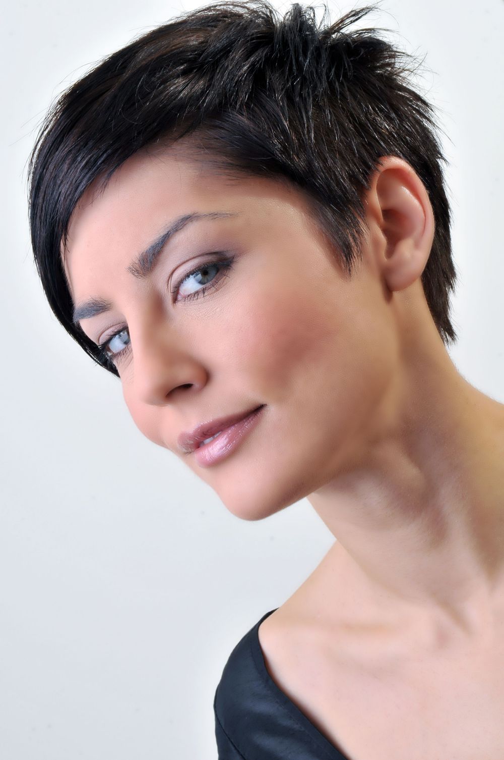 Close-up portrait with short dark pixie haircut and natural makeup against light background.