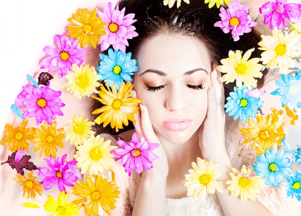 Portrait with colorful daisies surrounding woman with closed eyes and peaceful expression.