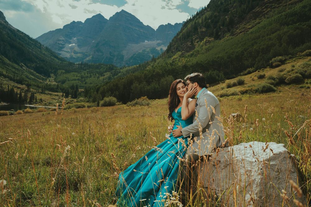 Couple in formal attire sharing romantic moment in mountain meadow setting.