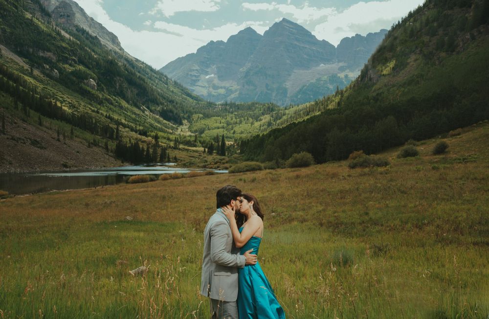 Romantic couple embracing in scenic mountain valley with turquoise dress and grey suit.