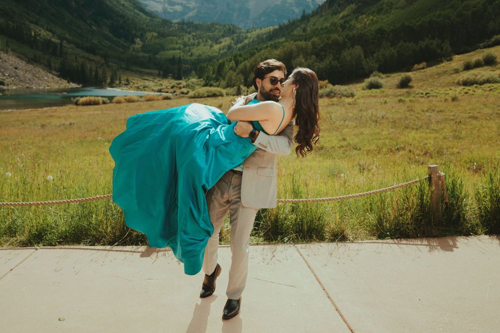Playful dancing couple in mountain valley with flowing turquoise dress.
