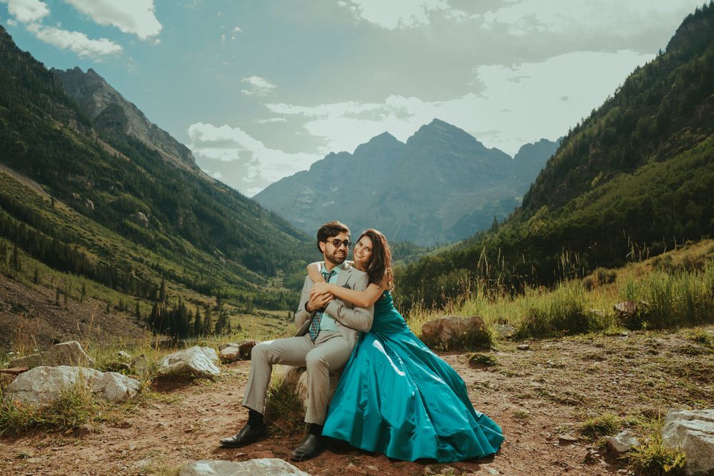 Couple sitting on rocky ground with majestic mountain vista in background.