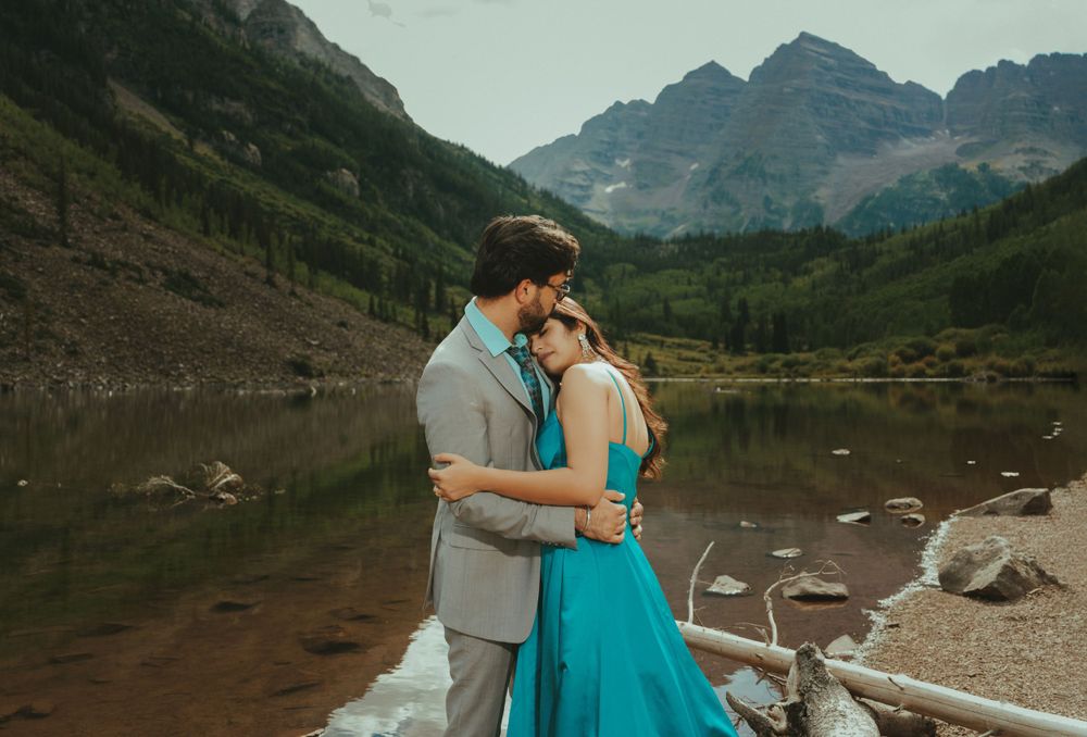 A romantic embrace by an alpine lake with mountain peaks and reflections in the still water.