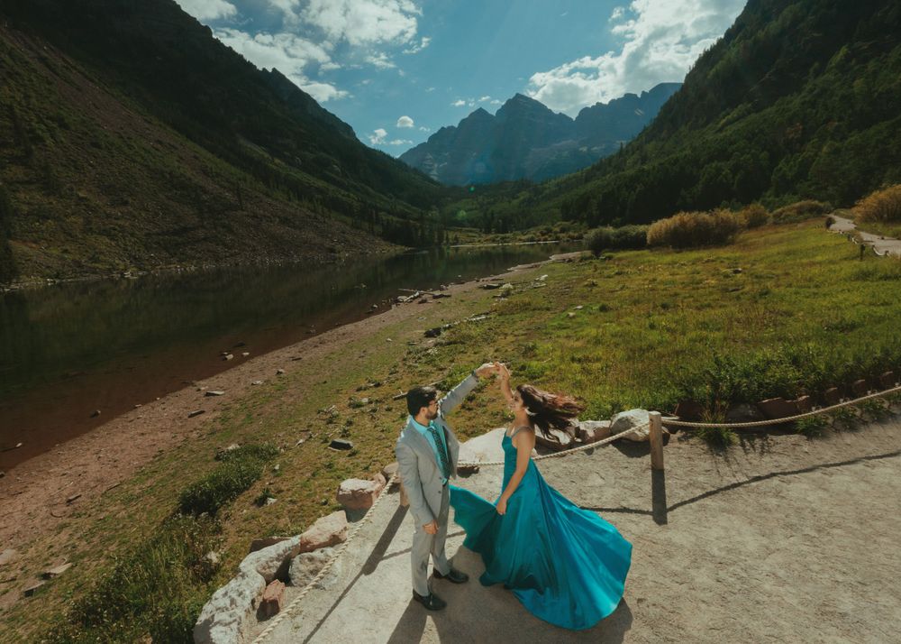 A flowing turquoise dress twirls against rugged mountain scenery on a bright mountain path.