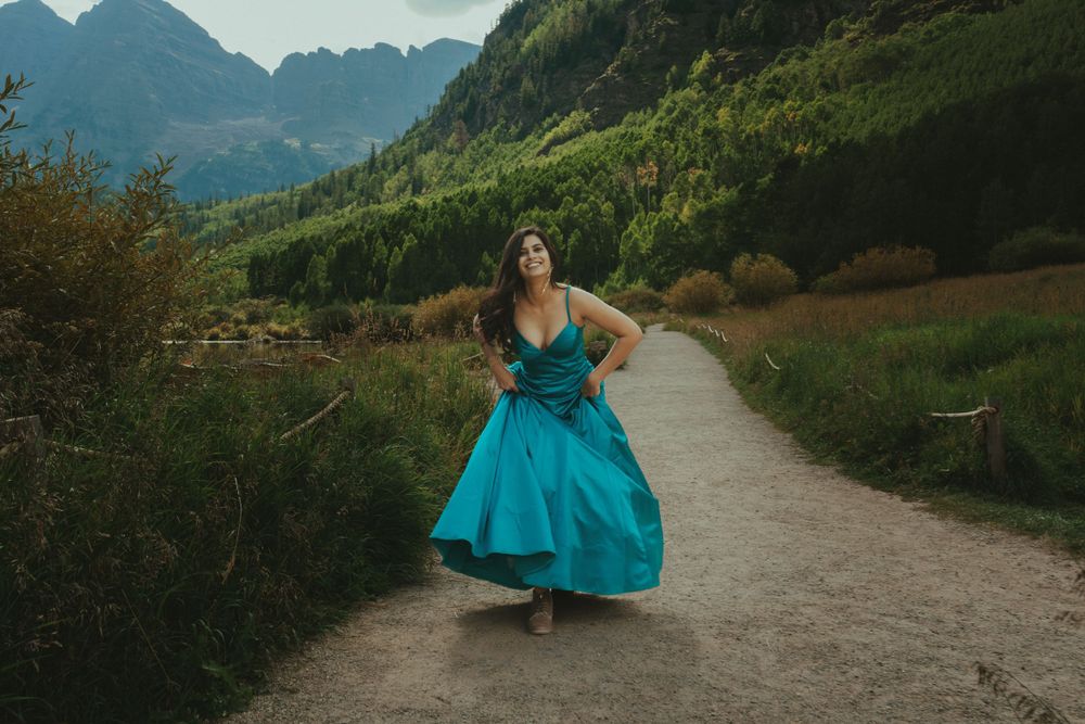 Woman in flowing turquoise dress twirling on mountain path during sunset.