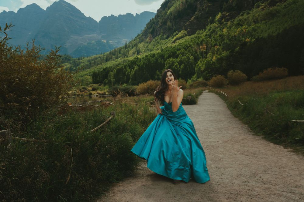 A turquoise ballgown illuminates a mountain path during a dramatic outdoor photoshoot in nature.