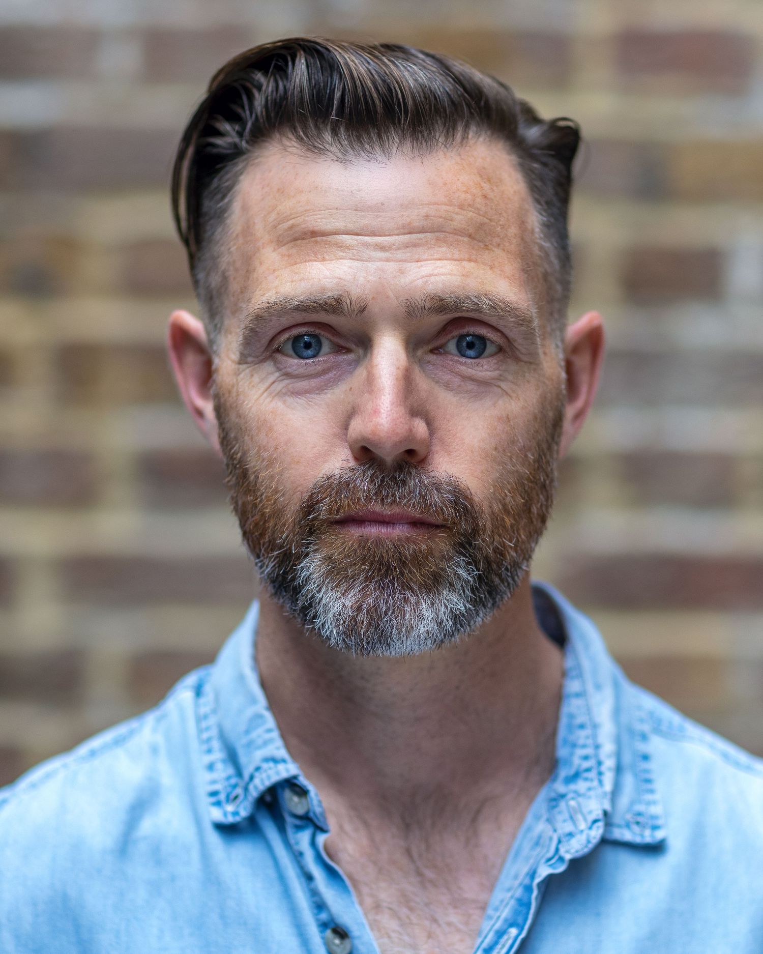 Actor Finn Hanlon looking directly into camera for his acting headshot against a brown brick wall