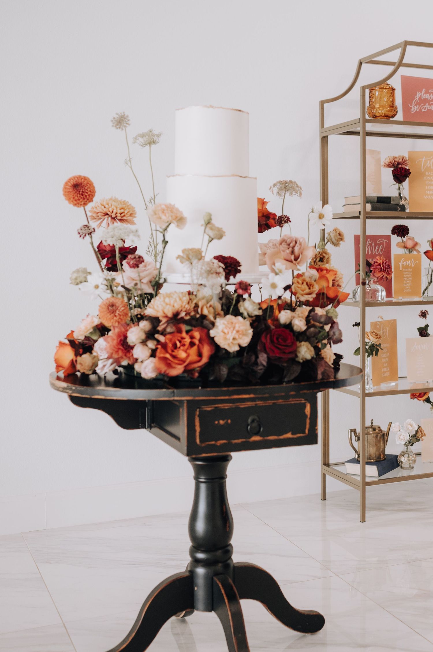 Vintage black side table featuring elaborate floral arrangement with coral and burgundy blooms.