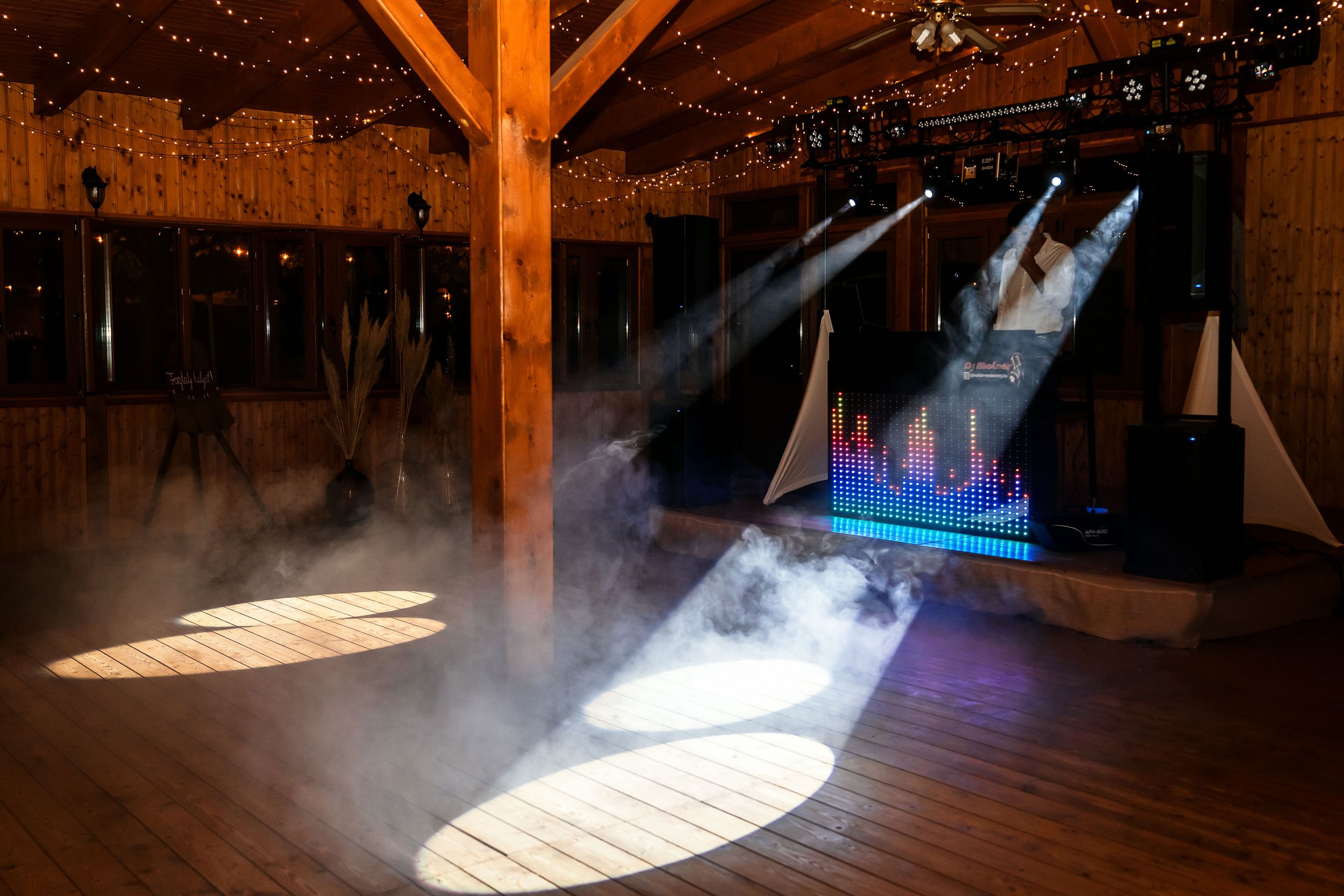 Empty dance floor with dramatic lighting and fog effects inside a rustic wooden barn venue.