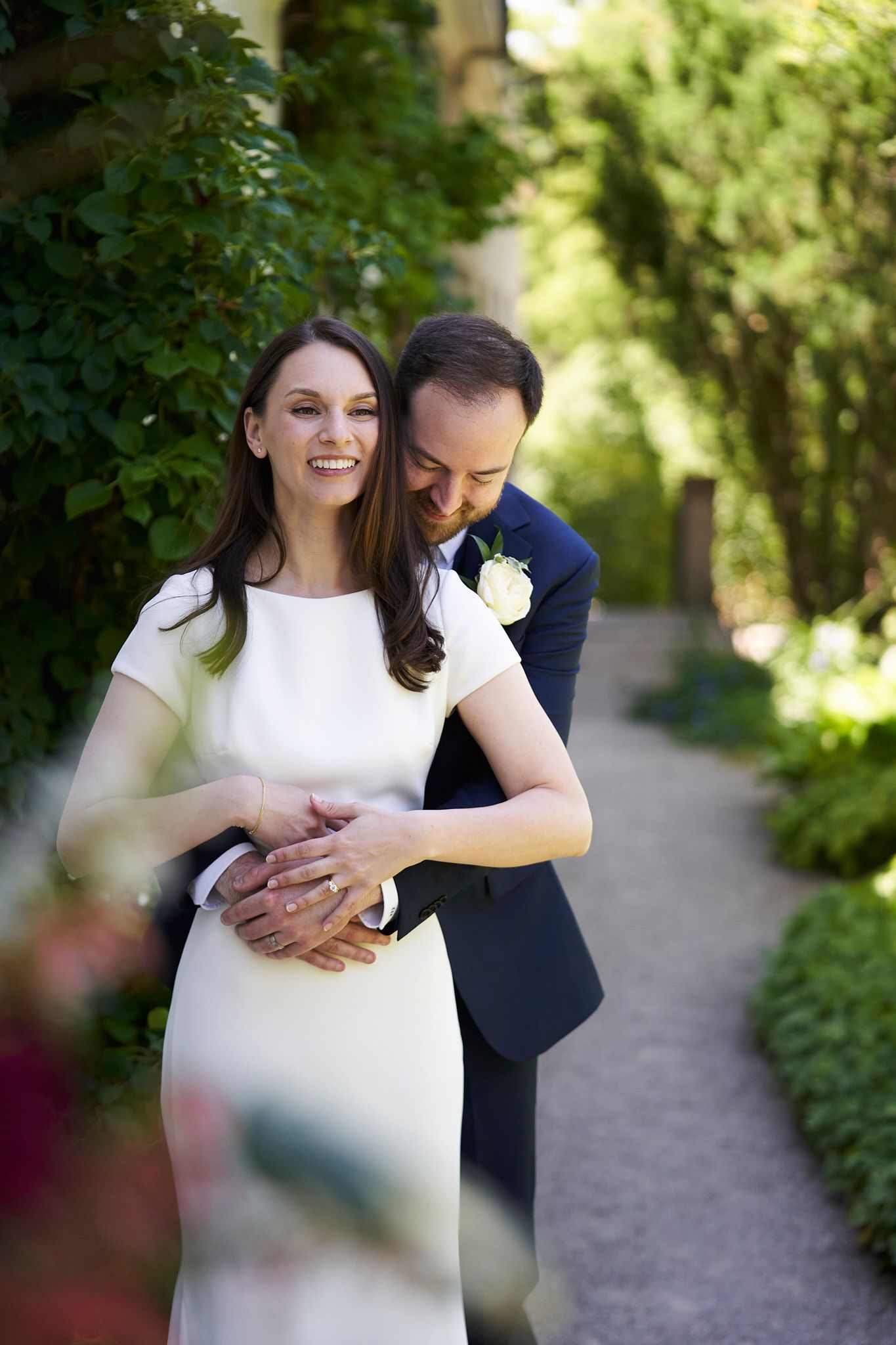A couple shares an intimate moment in a garden pathway wearing formal wedding attire for their wedding at Langdon Hall.