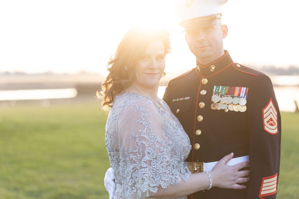 Beautiful bride in lace gown posing with Marine groom in dress uniform at golden sunset.