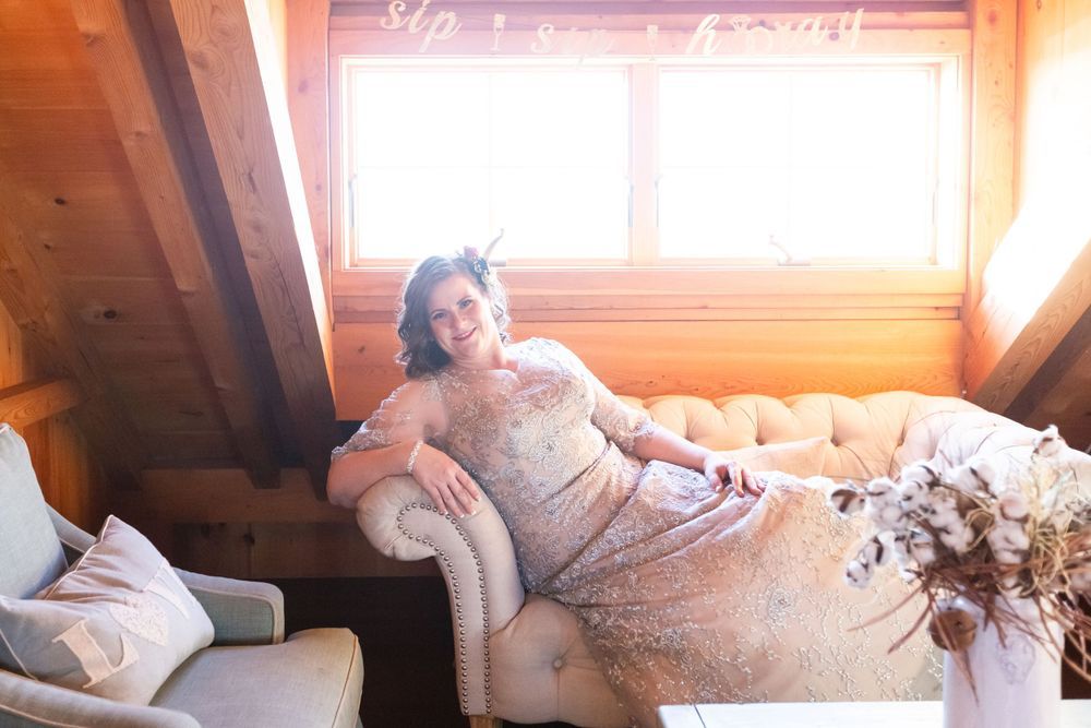 Radiant pregnant woman in lace gown reclining on vintage sofa in a warm rustic wood cabin.