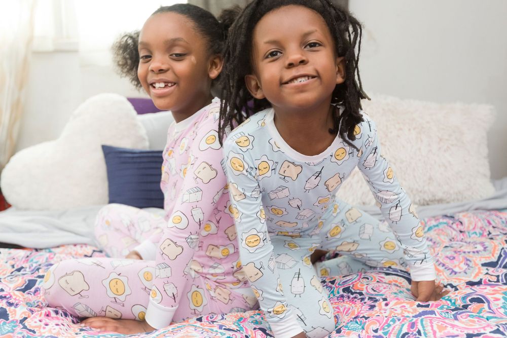 Two young girls in colorful pajamas sitting together on a bed with rainbow bedding.