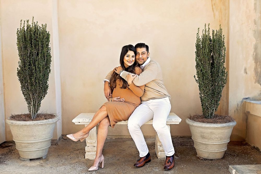 Happy couple sitting close together on a bench with potted topiaries against a warm beige wall.