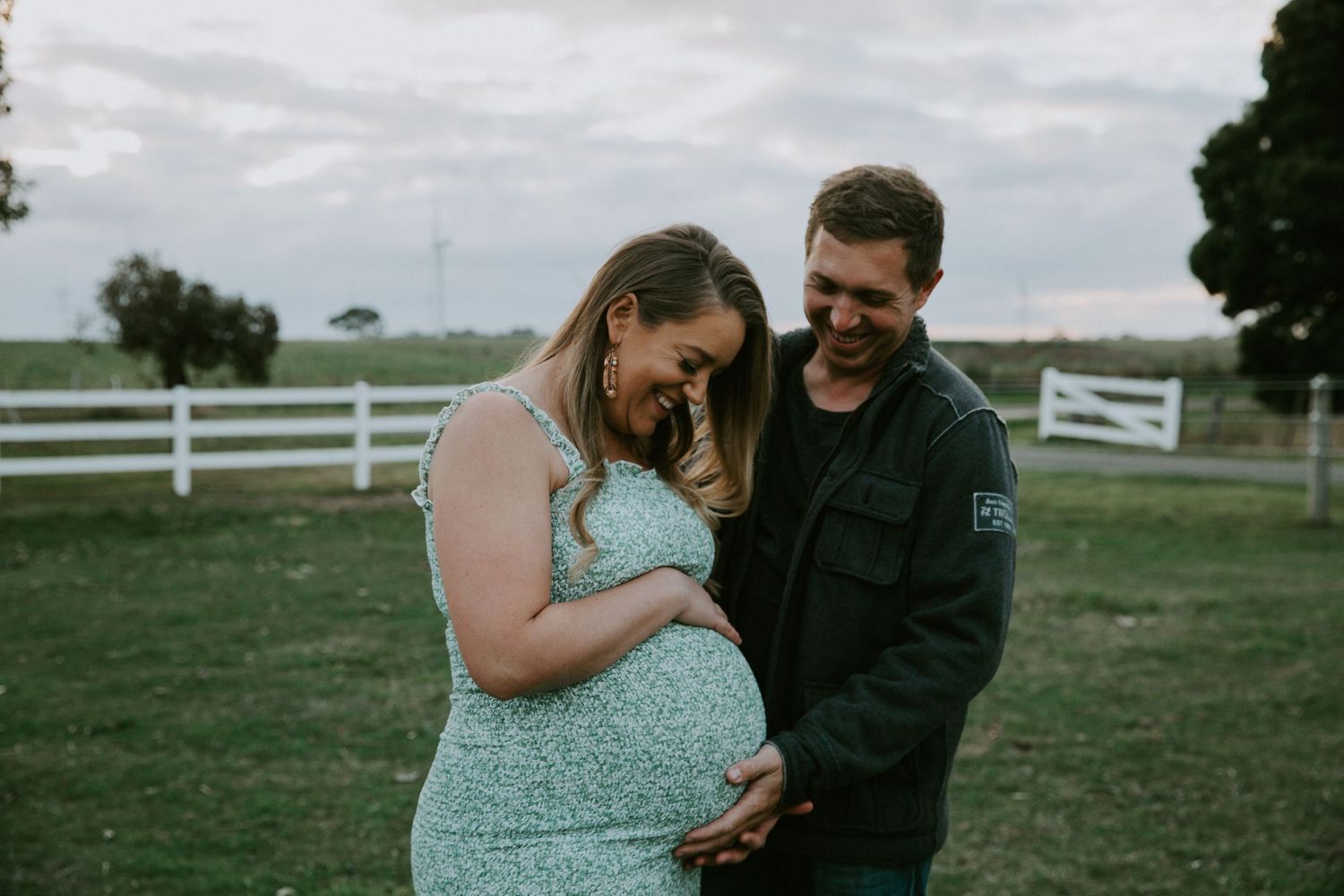 A couple shares tender moments in a field with white fences, captured in a series of romantic outdoor photographs.