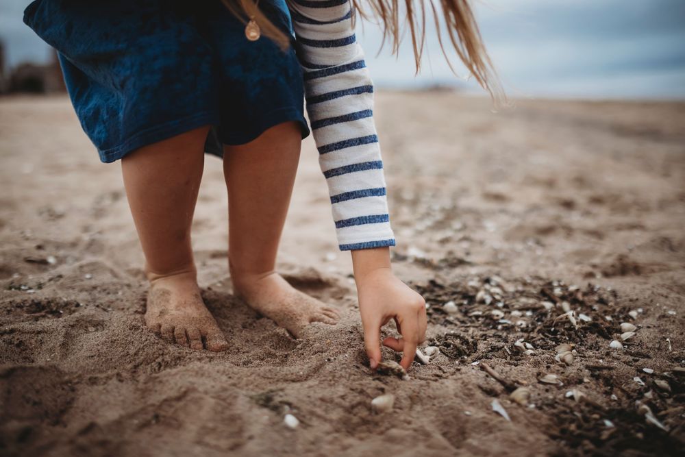 Close-up of feet and hands playing in wet beach sand with striped sleeve visible.