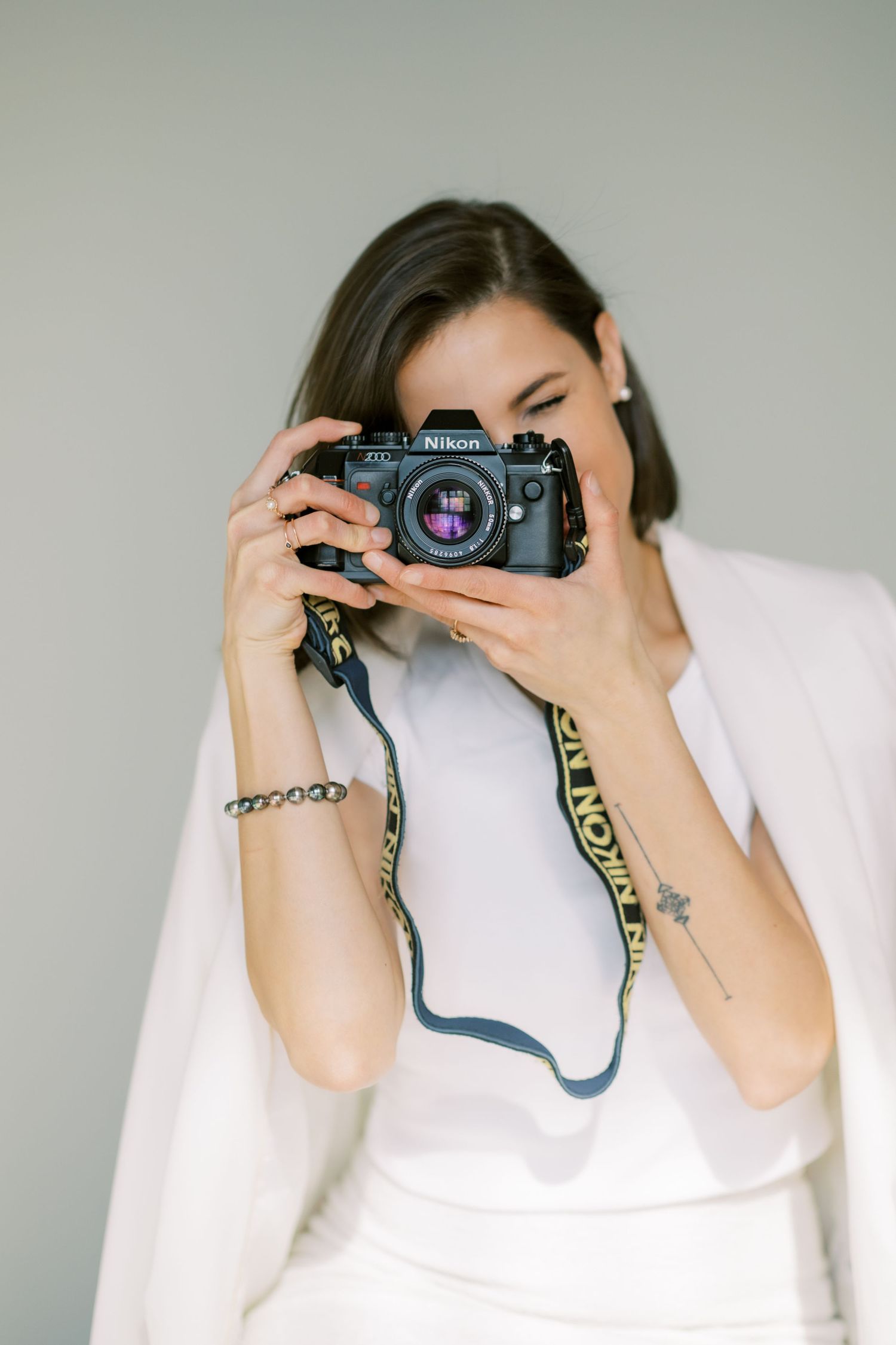 Someone holding vintage Nikon camera wearing white top against gray background.