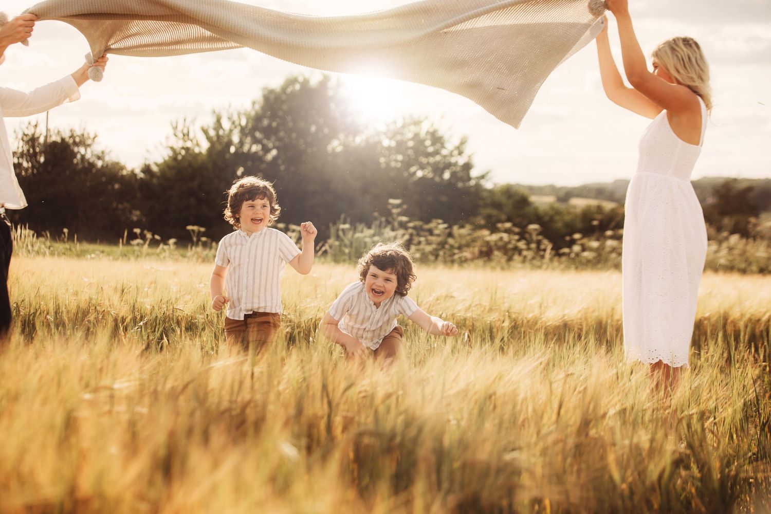 Family holding white fabric in golden field at sunset with sunlight streaming through.