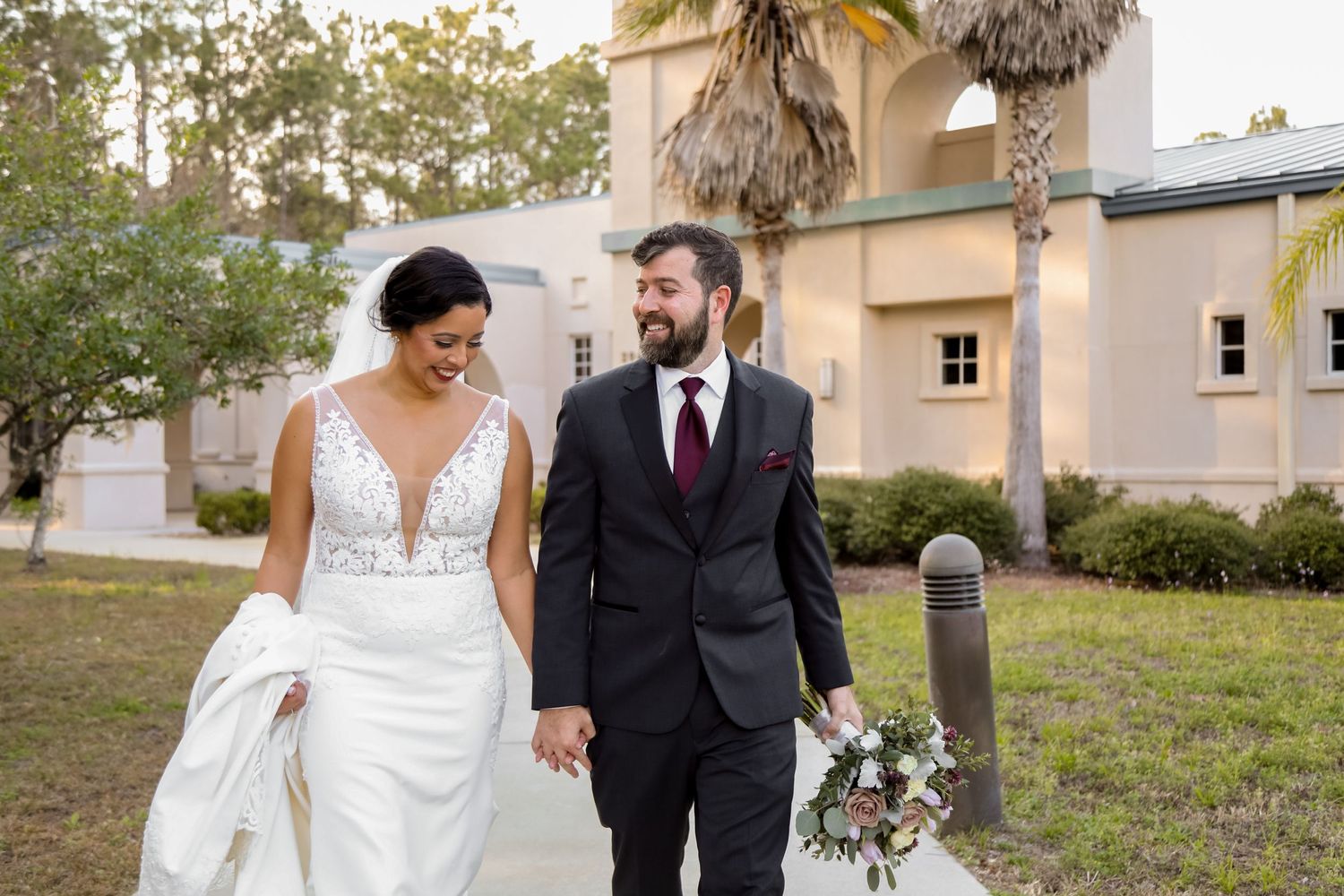 Couple walks together on outdoor path holding wedding bouquet.