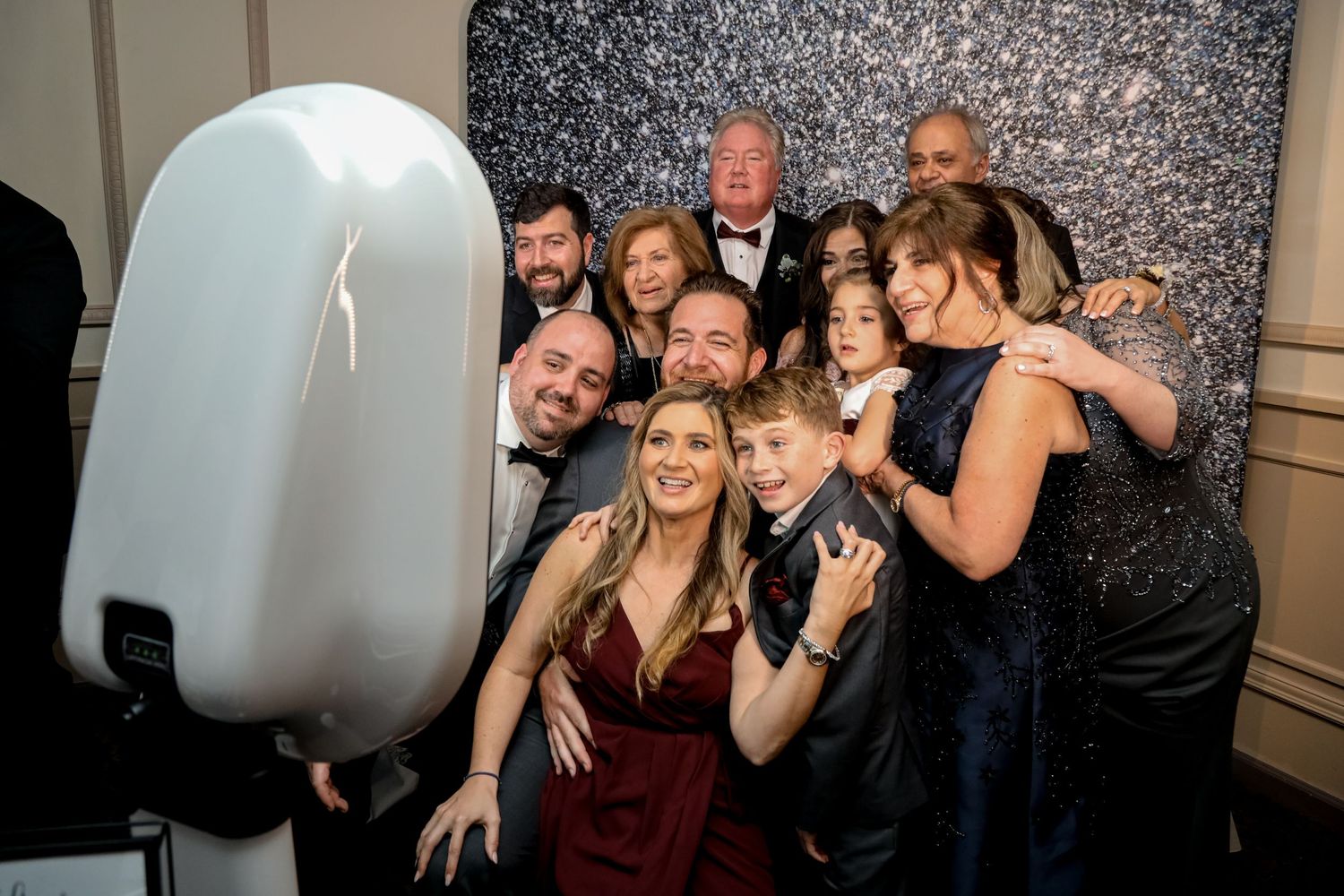 Wedding party poses together with photo booth and sparkly backdrop.