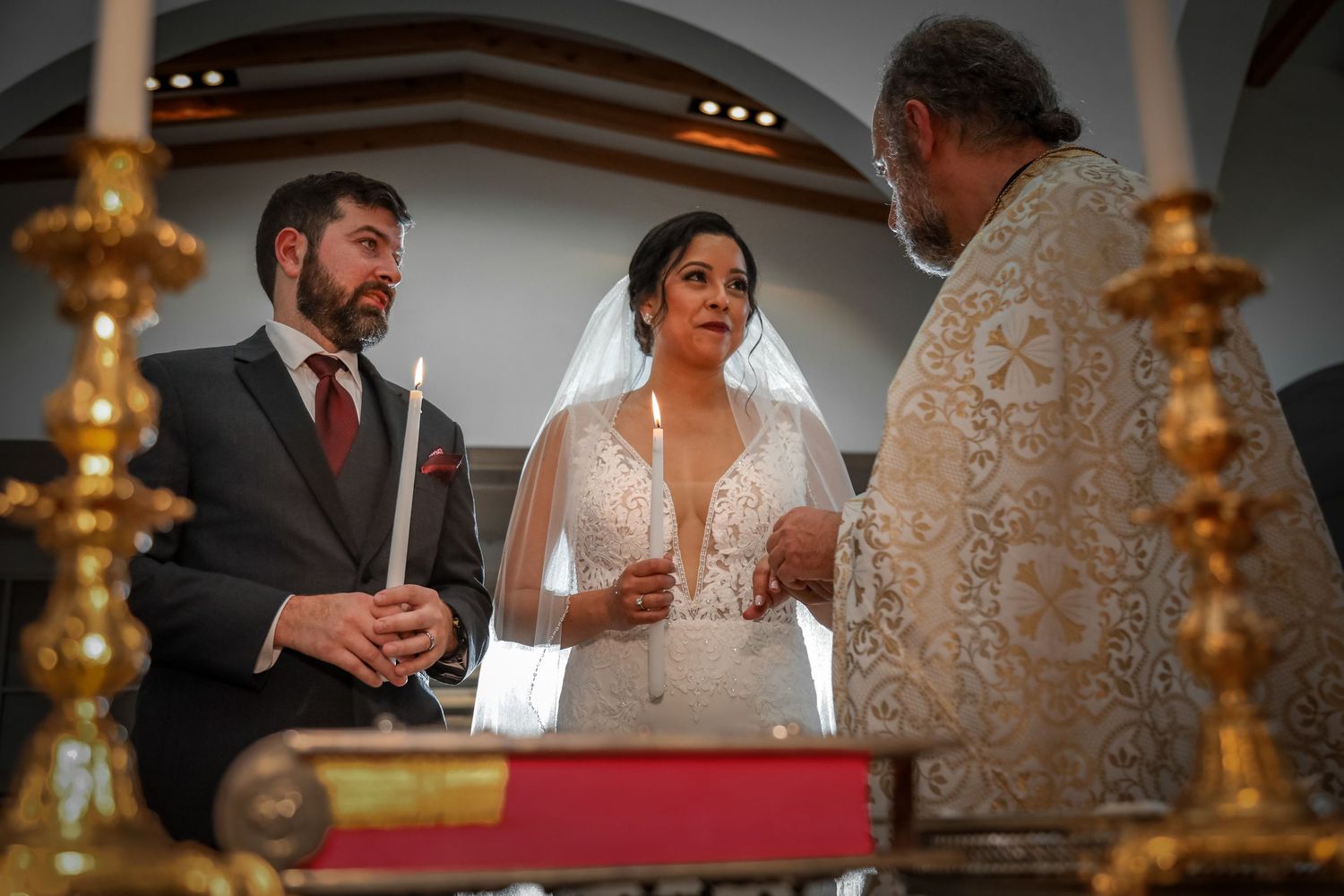 Wedding ceremony in progress inside ornate church with gold candelabras.