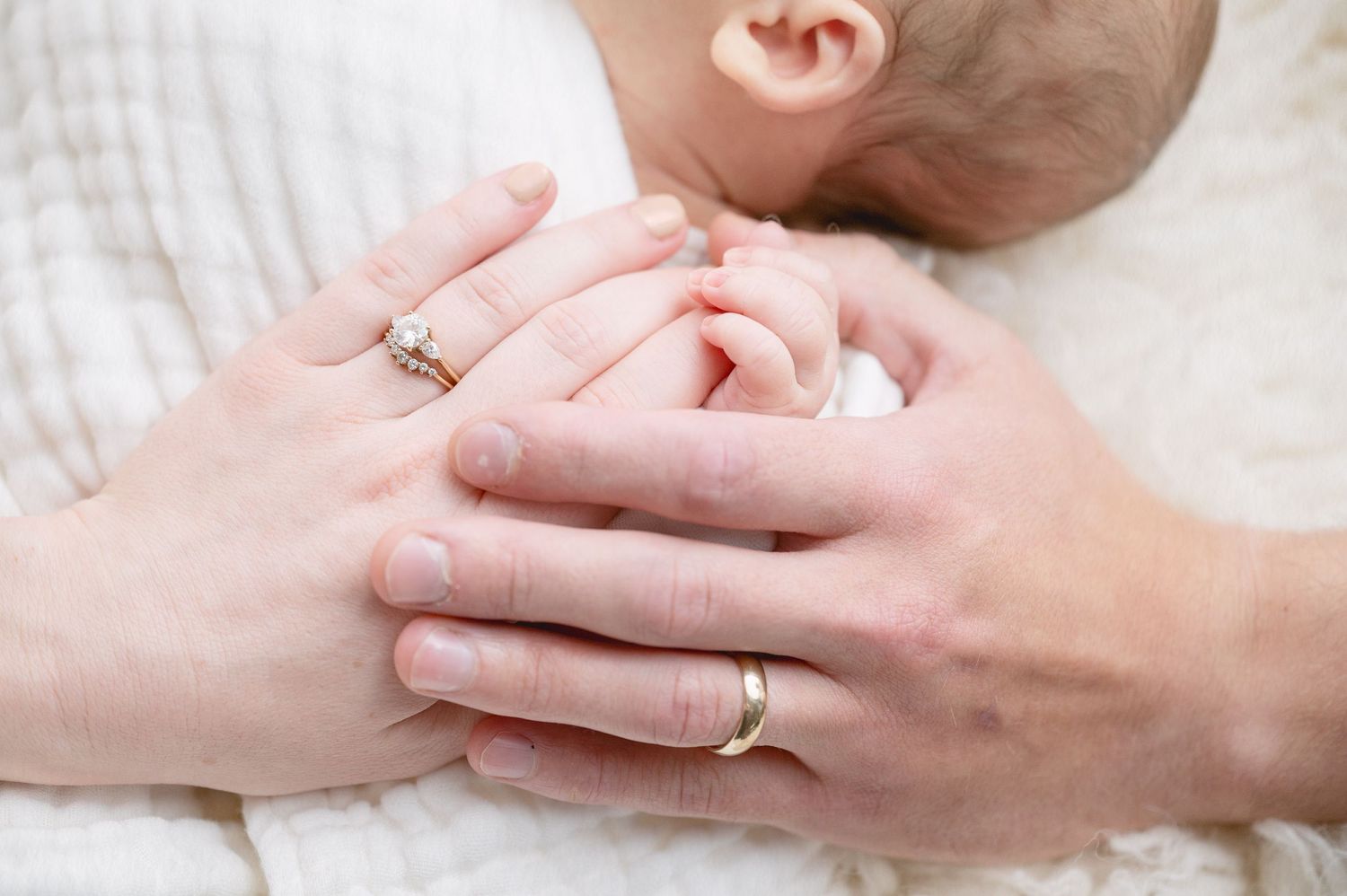 Gentle hands with wedding rings cradling a newborn baby.