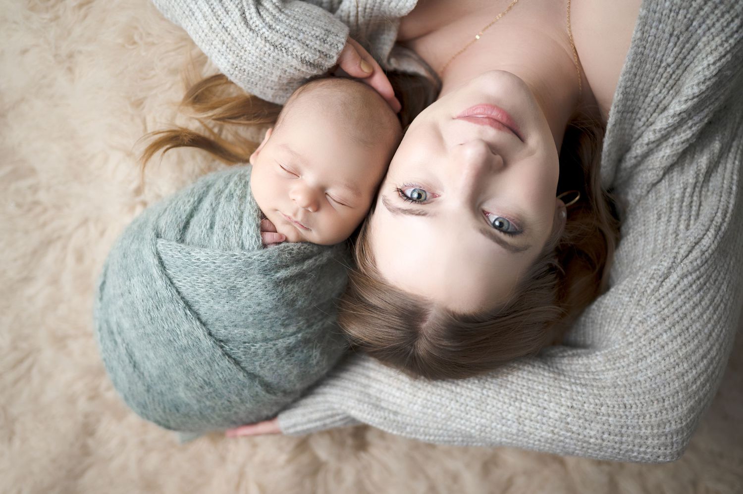 Overhead view of parent and newborn lying together on plush carpet.
