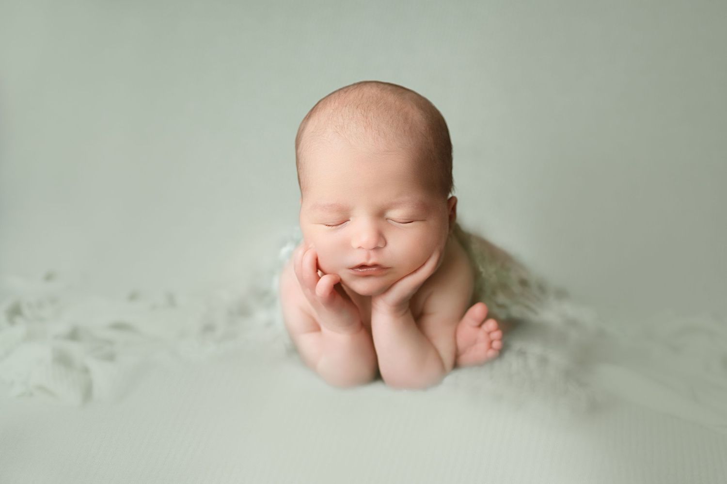 Sleeping newborn baby posed in frog position on soft white backdrop during professional photoshoot.