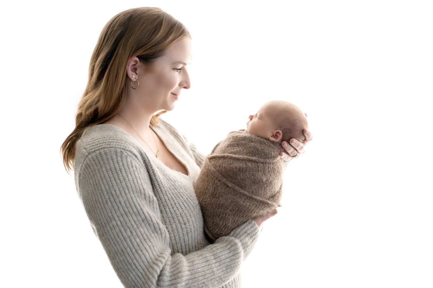 Parent in gray sweater holding swaddled newborn against white background.