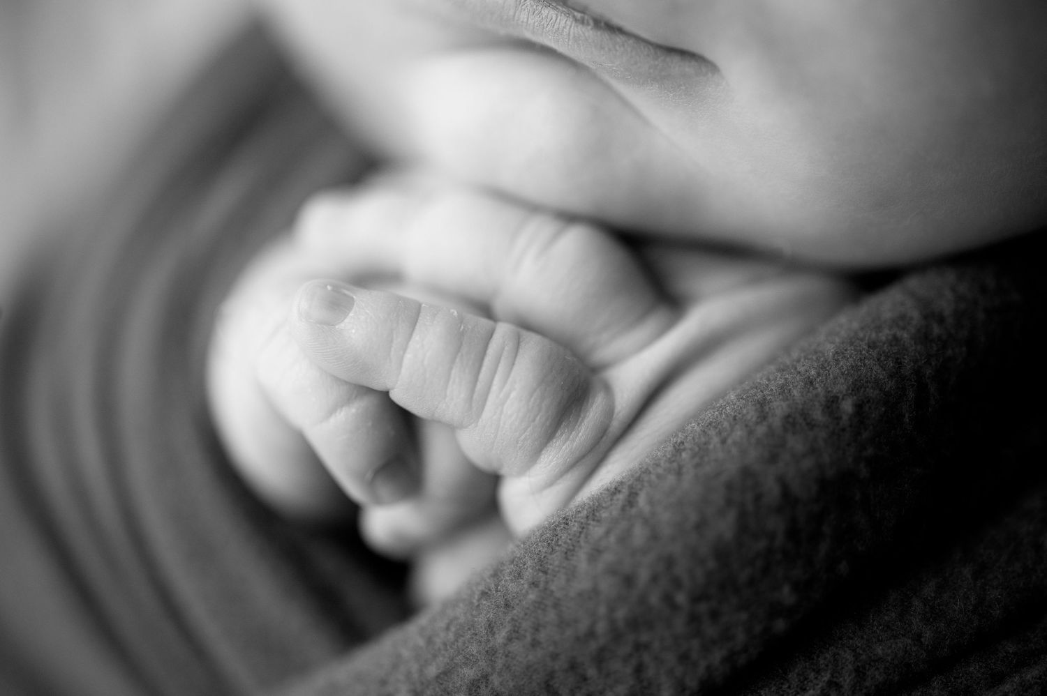 Close-up black and white image of a baby's tiny hand resting on soft fabric.