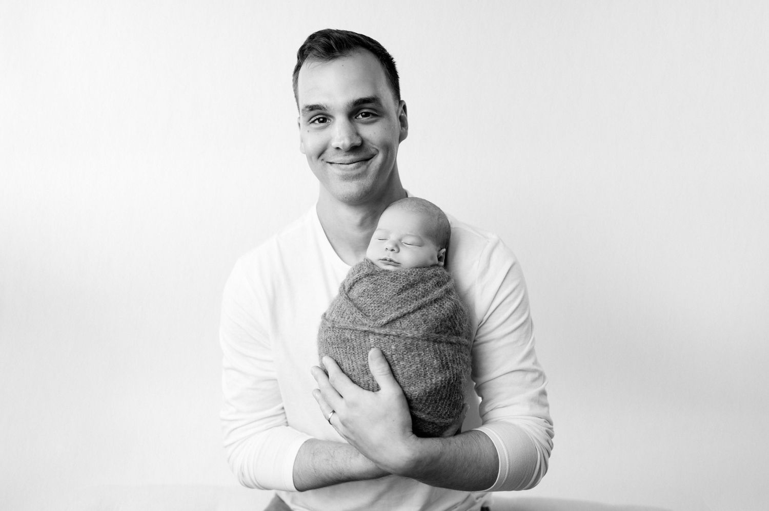 Portrait of parent holding sleeping newborn wrapped in gray blanket against white background.