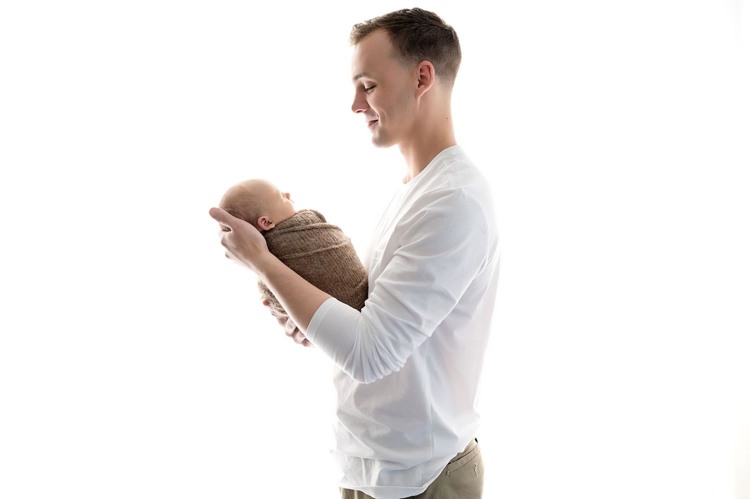 Parent in white shirt tenderly holding swaddled newborn against light background.
