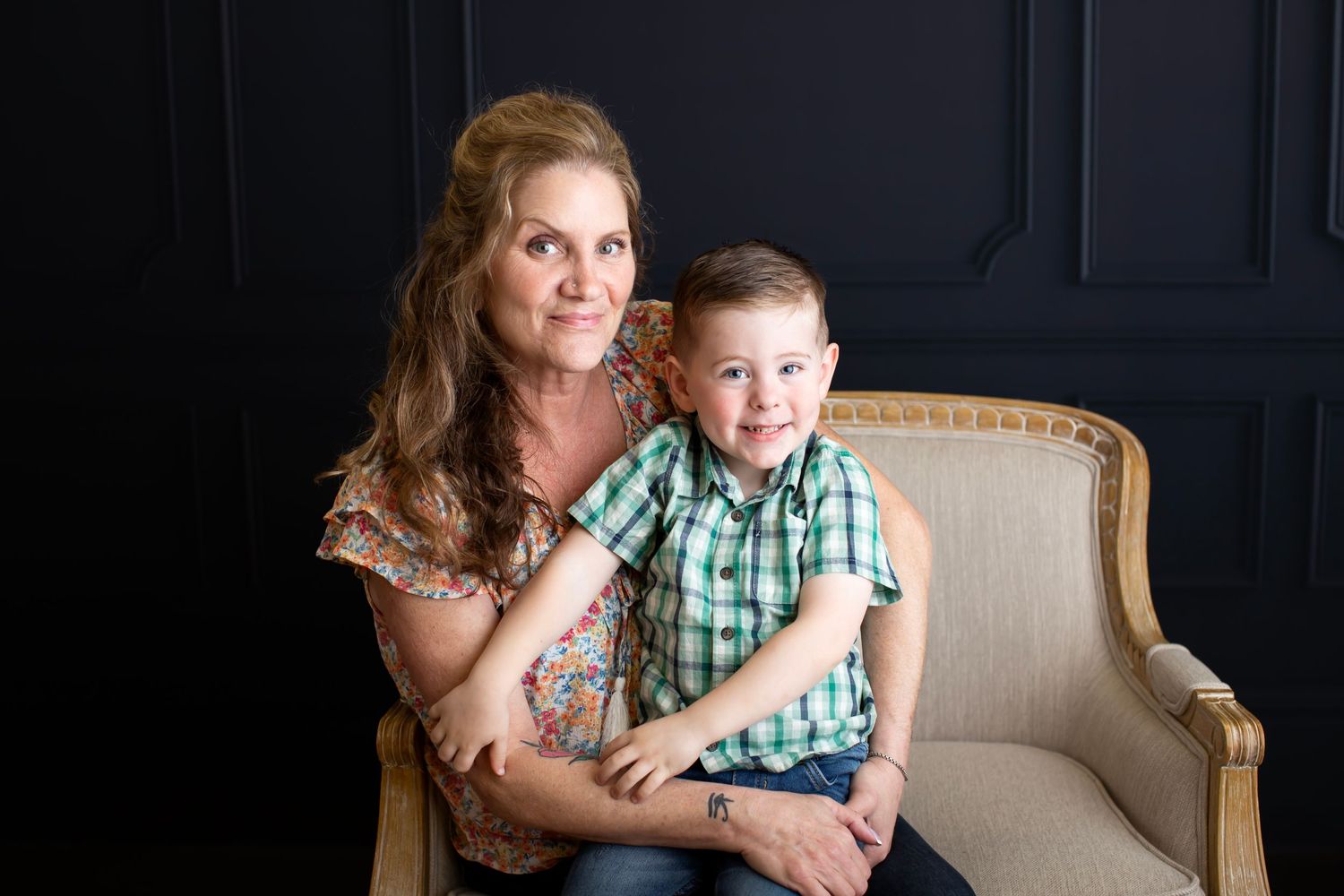 Intimate portrait session on beige armchair against dark backdrop.