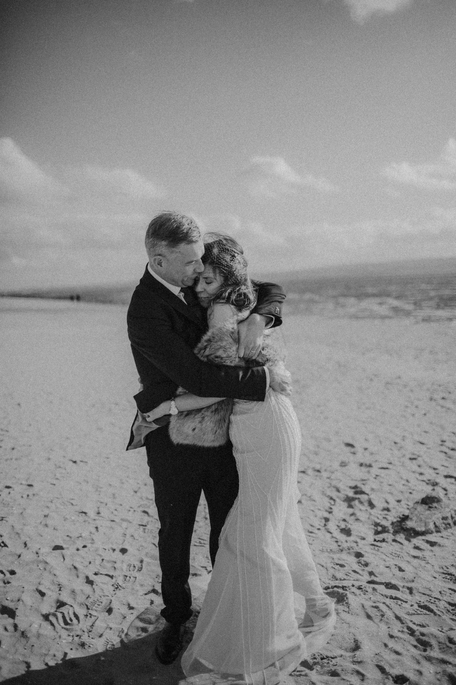 A black and white beach wedding photo capturing an intimate embrace.