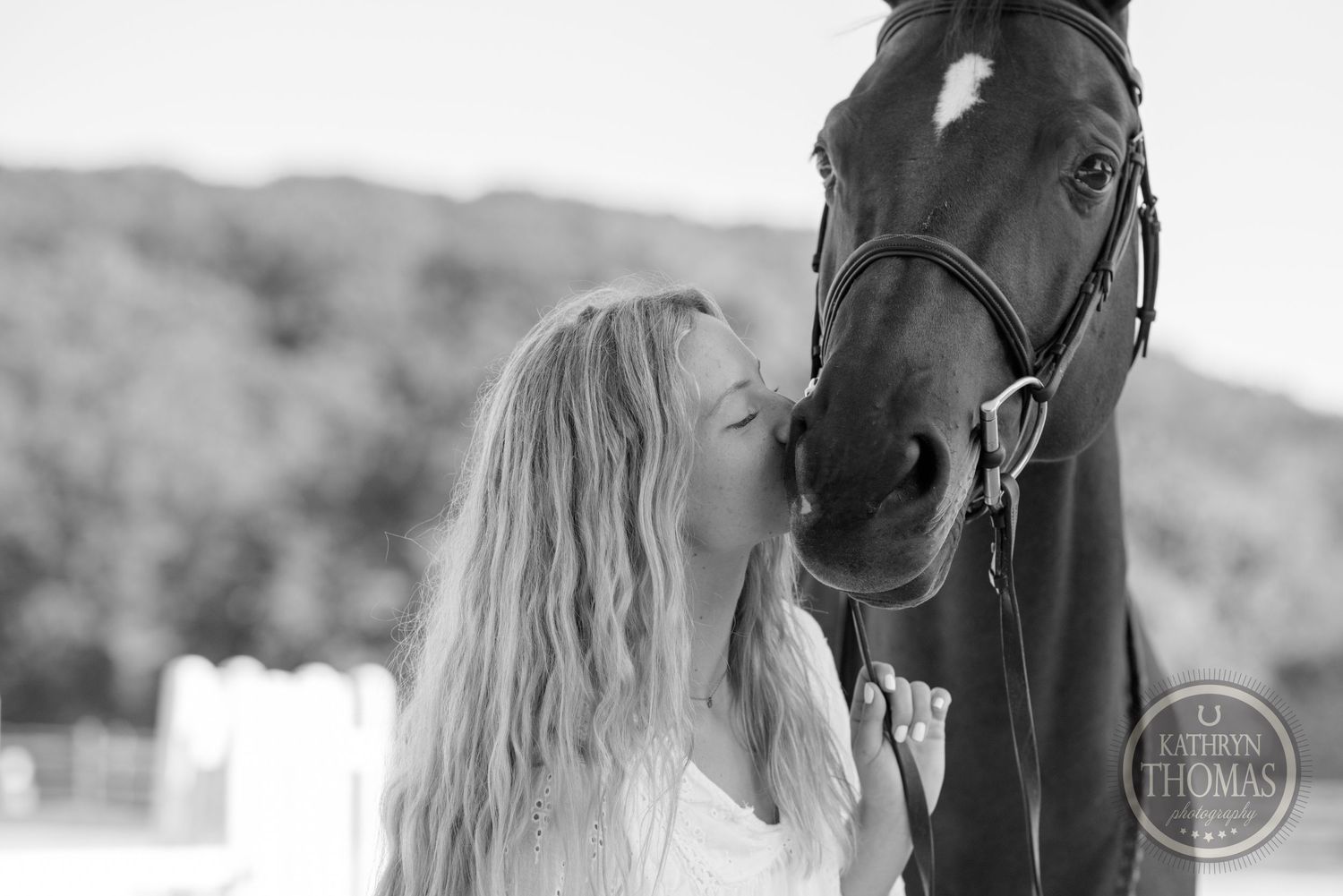 Black and white intimate portrait of person connecting with horse against mountain backdrop.