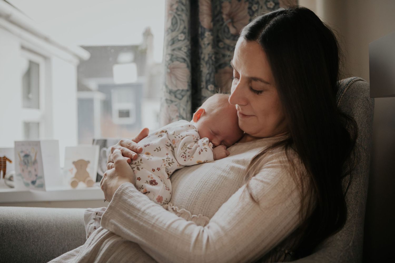 New born at home photo shoot with Cornwall new born photographer mum sat with baby in window