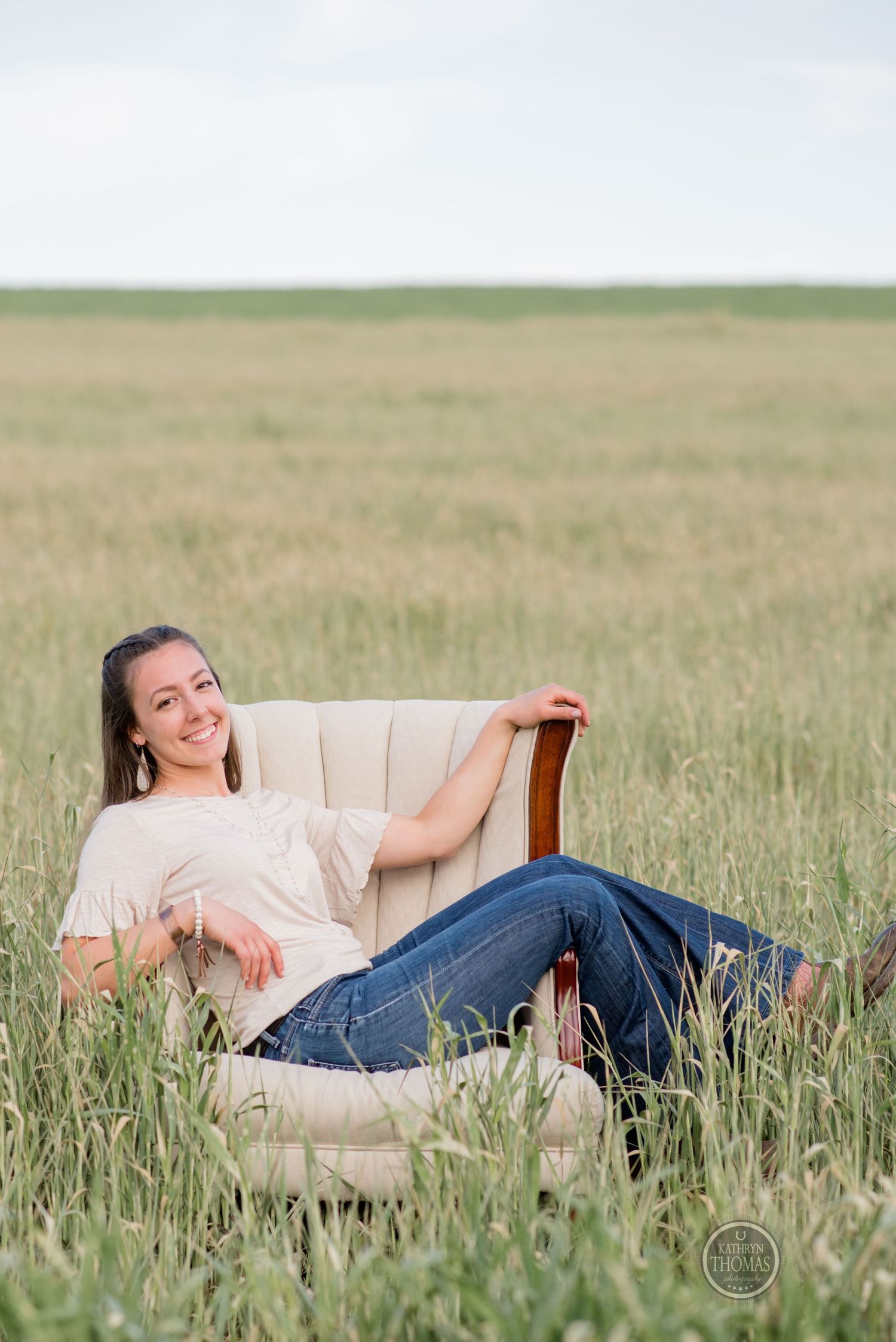 A beige armchair placed in a grassy meadow with someone lounging casually.