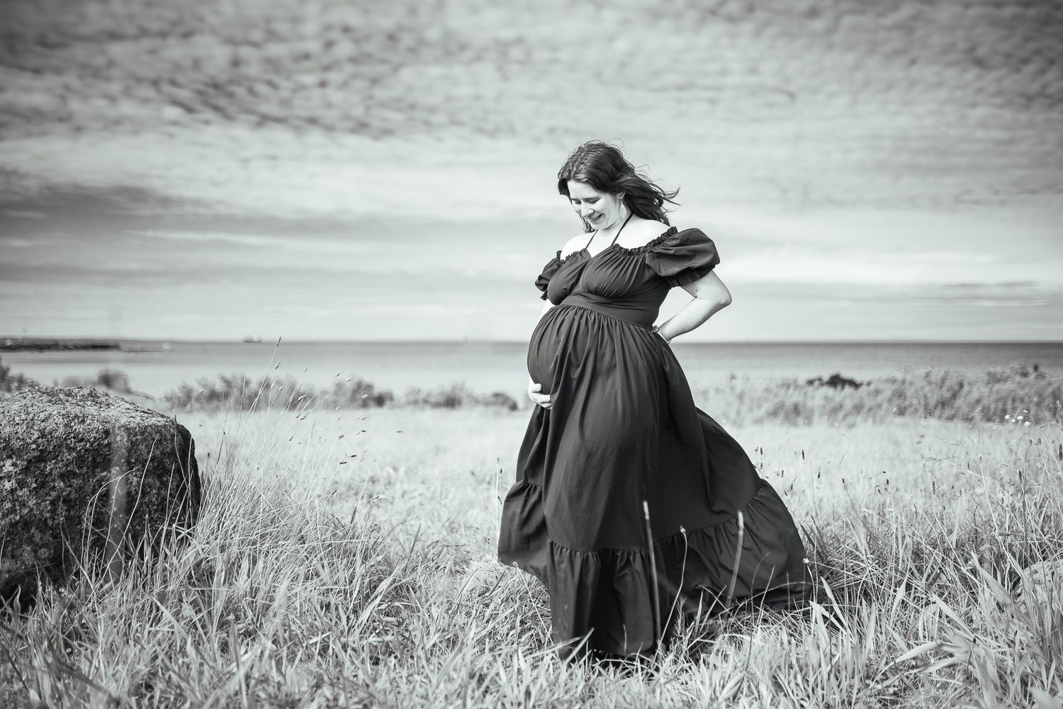 Pregnant woman in flowing dress standing in coastal field, black and white photo by Pei A Photography, a Melbourne Maternity Photographer.