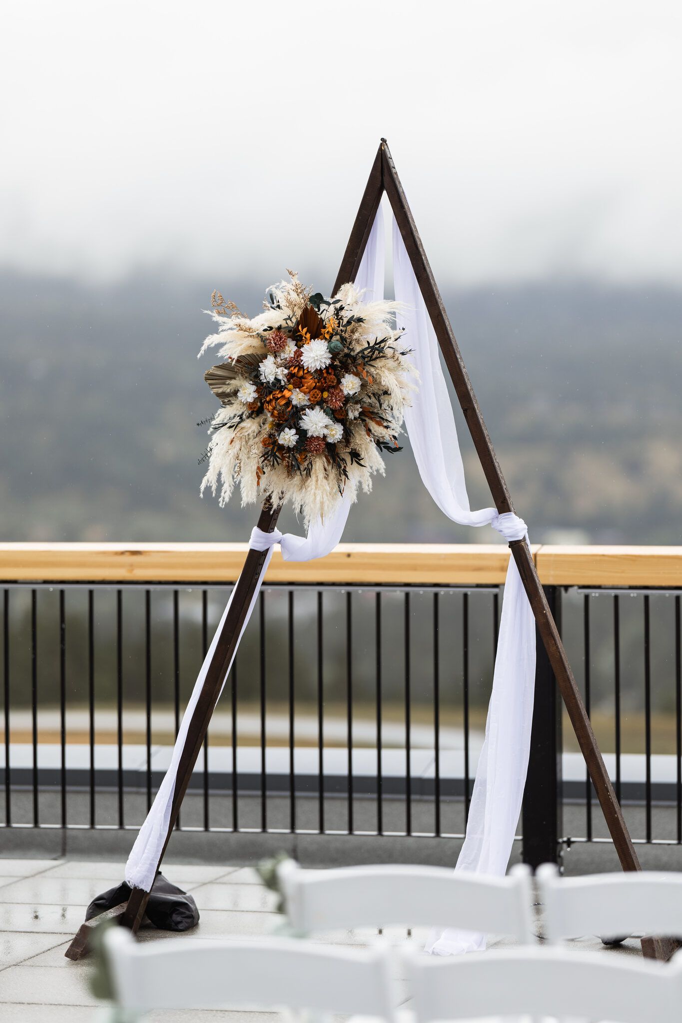 Triangular ceremony arbor with dried florals and white draping on the Vista Canmore terrace