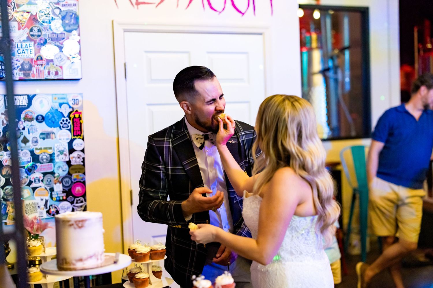 Bride and groom share a joyful cake tasting moment at their colorful wedding reception venue.