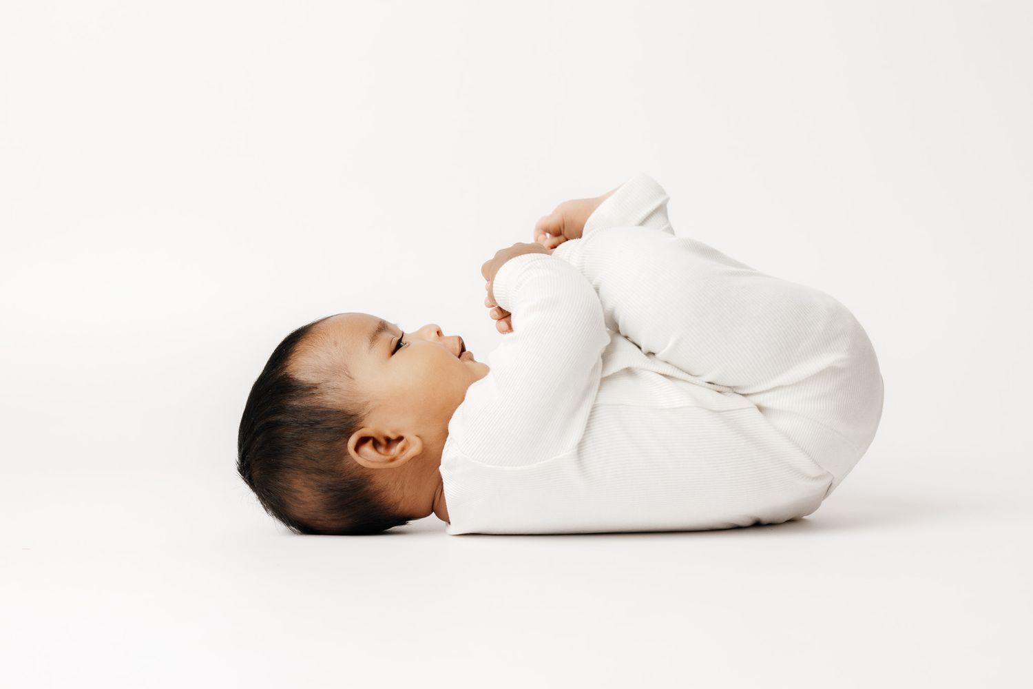 Peaceful newborn baby sleeping on white blanket, dark hair, soft skin, serene expression, professional newborn photography.