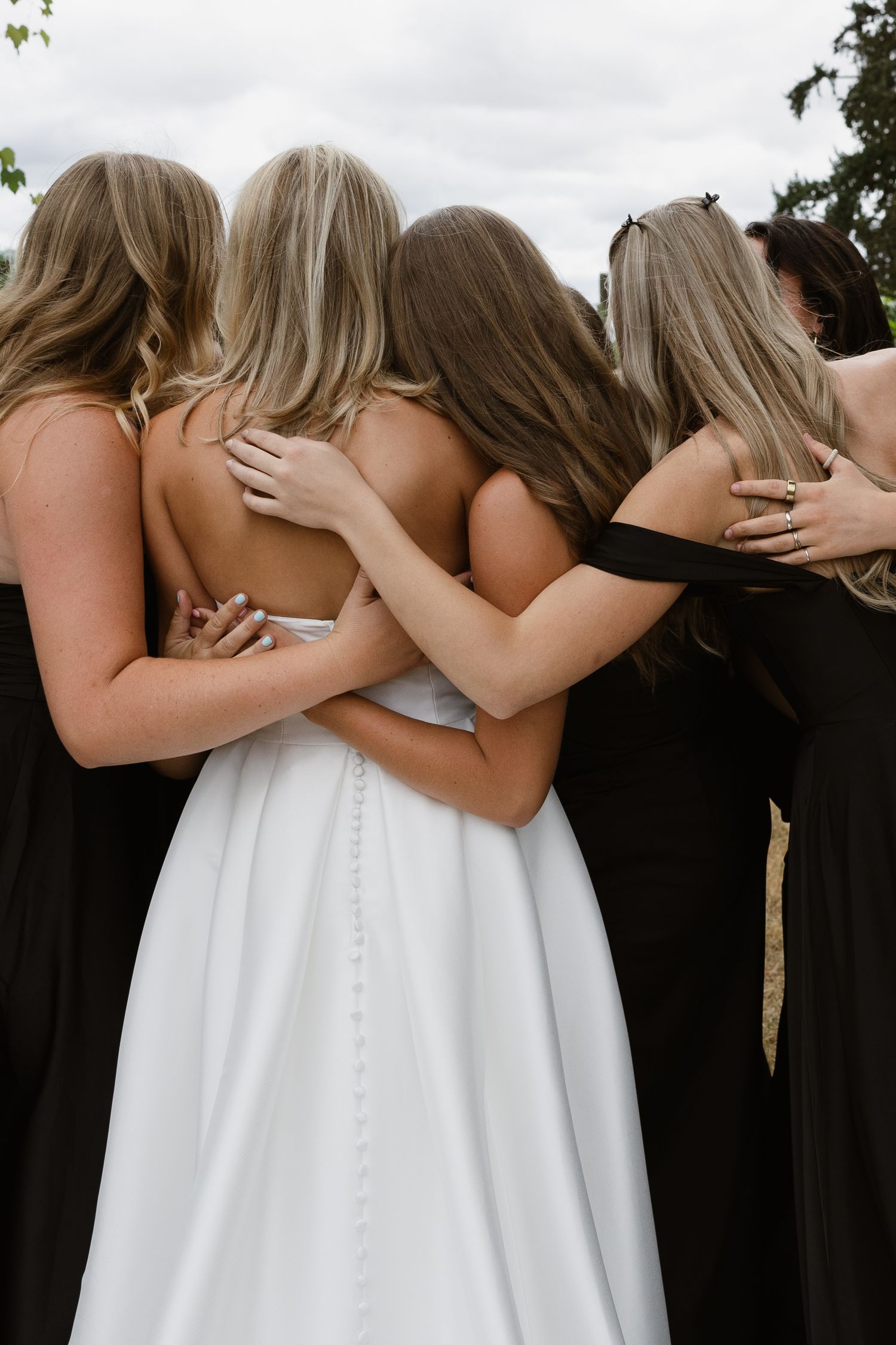 Bride in white gown holding white floral bouquet with pink ribbons, flanked by groomsmen in tan suits at wedding ceremony.