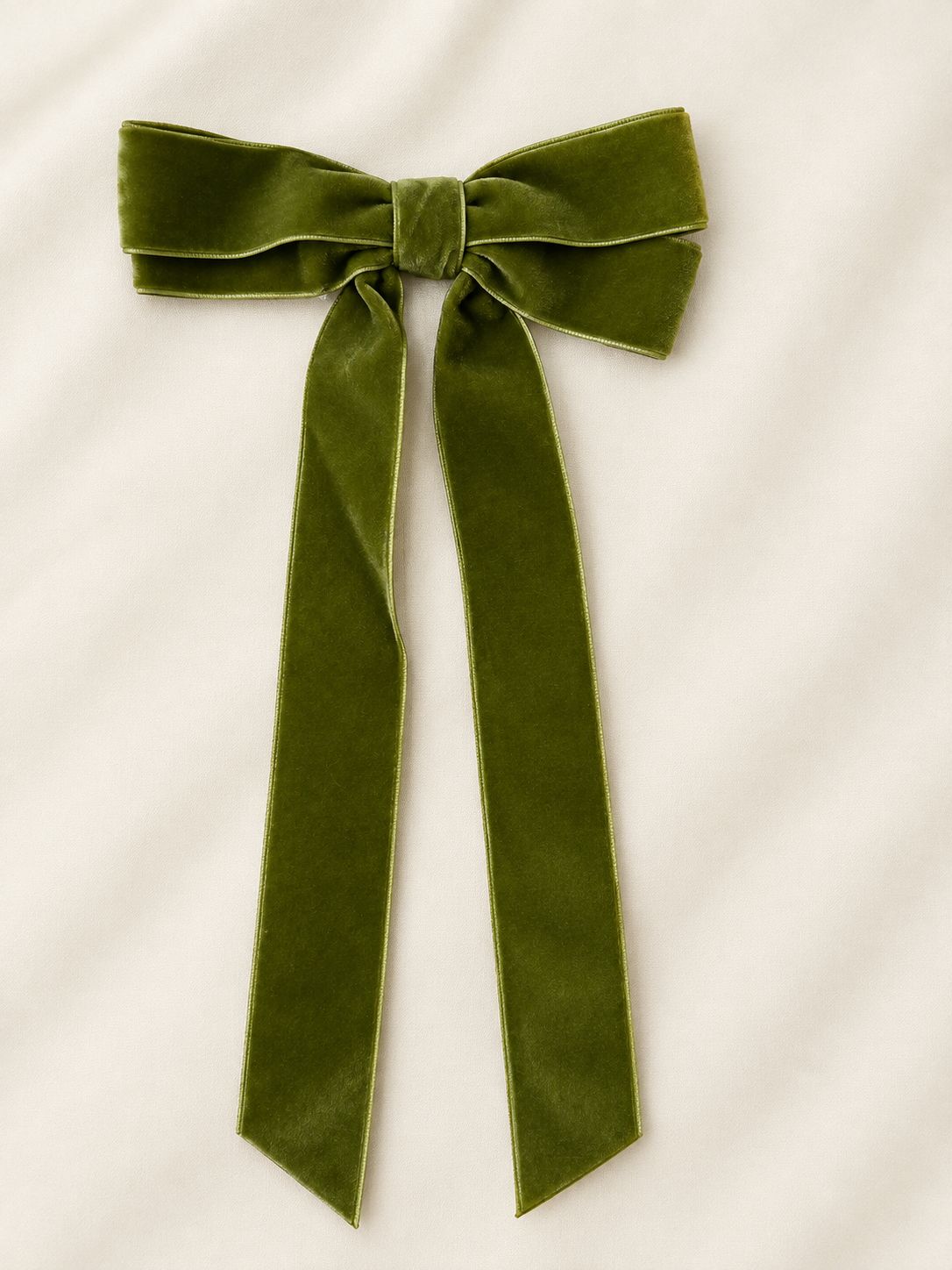 Olive green velvet hair bow with long trailing ribbons on a cream background.