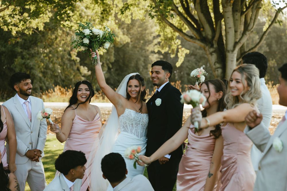 Bride and groom embrace in golden sunset light in an open field, wearing white gown and black suit.