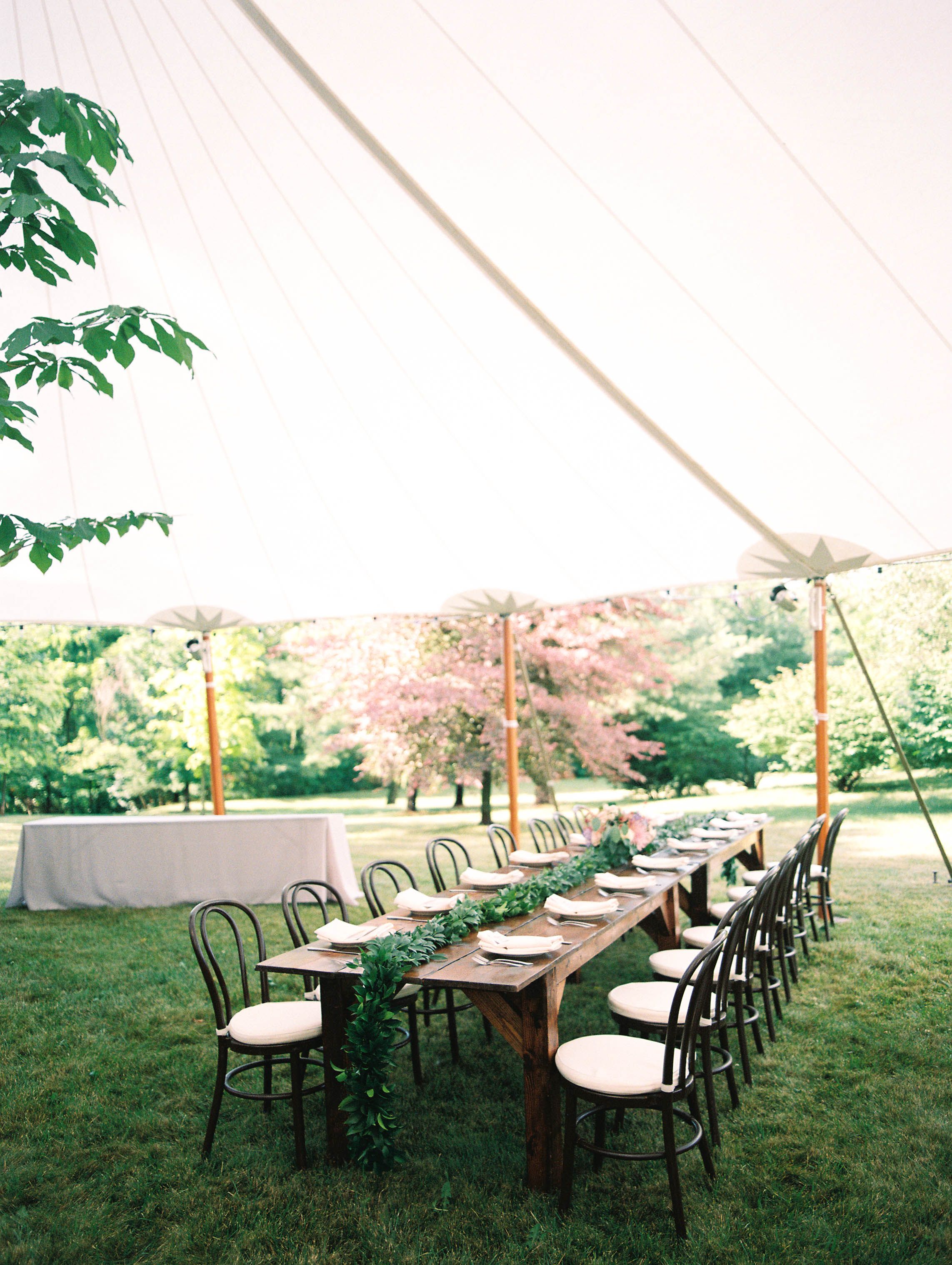 An elegant outdoor wedding reception setup with wooden tables under a white tent canopy.