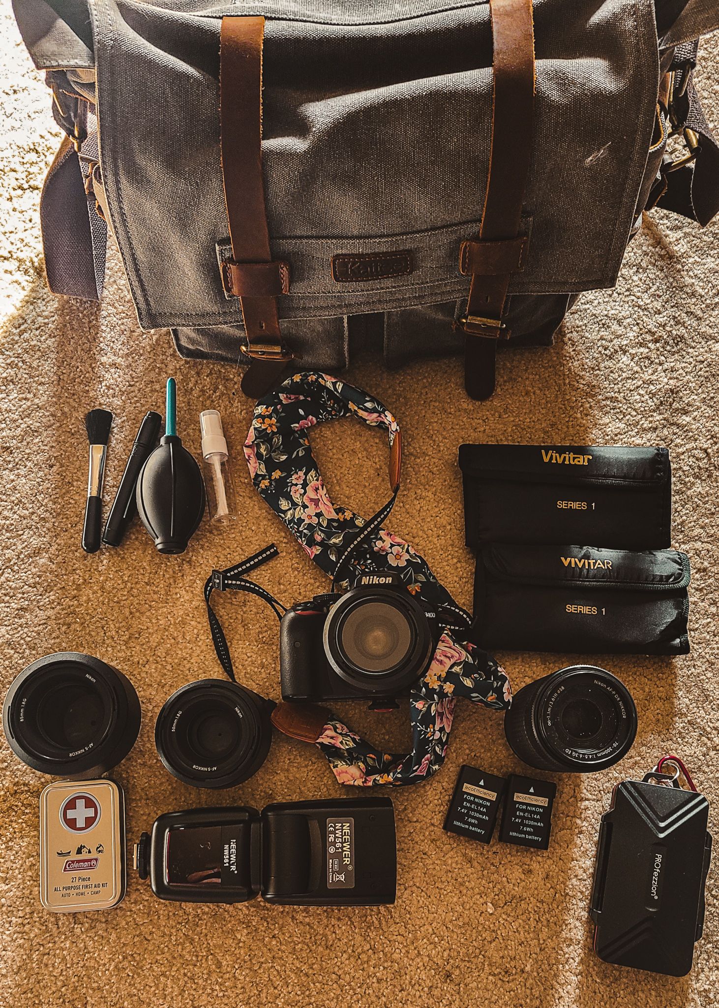 Photography equipment and accessories laid out next to a grey canvas messenger bag on carpet.