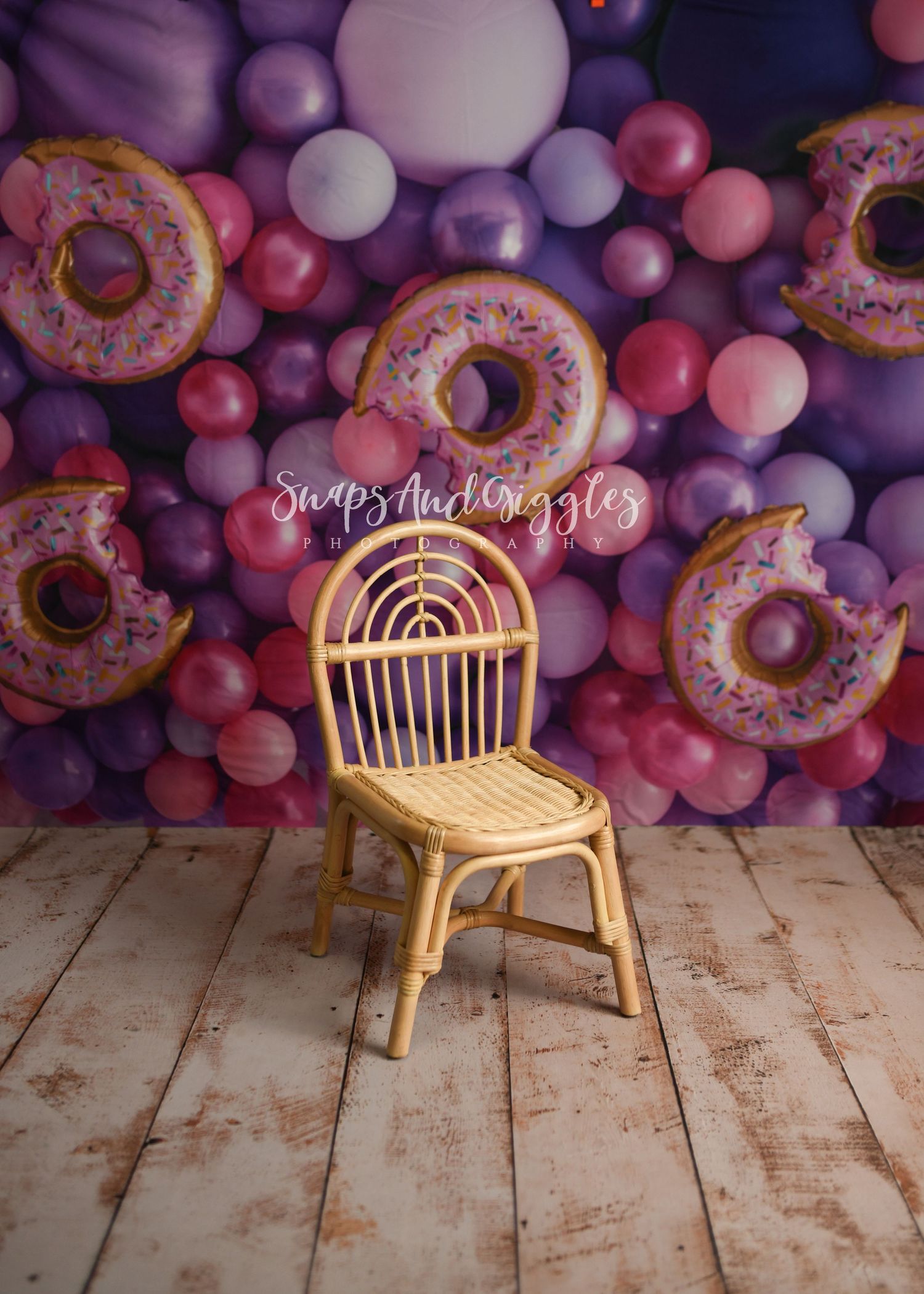Rattan chair against purple balloon wall with donuts creating whimsical photo backdrop.