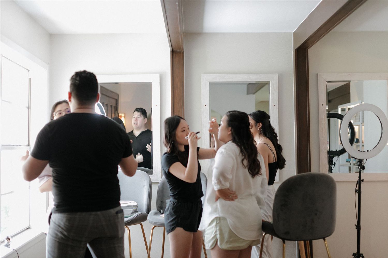 Wedding preparation scene with styling equipment and people getting ready in a bright room.