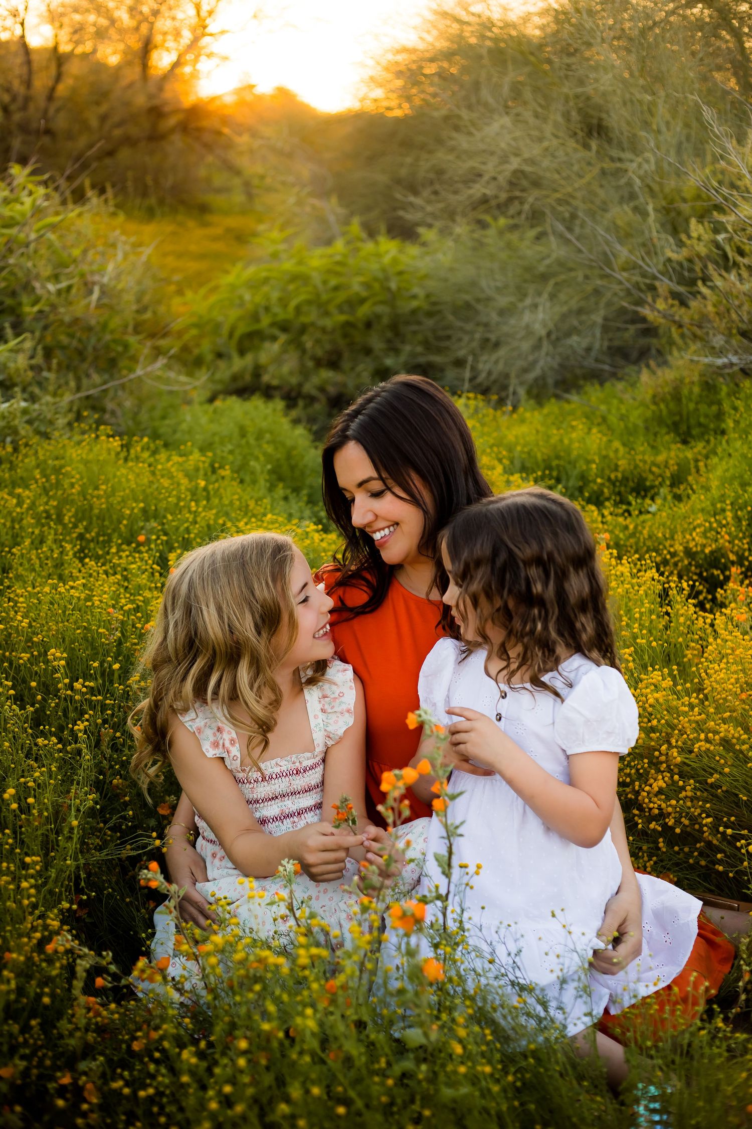 Mom and her two daughters snuggle in the flower field during sunset for a photo session to document motherhood.