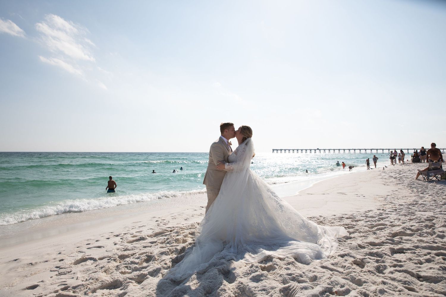 A romantic beach wedding moment captured with turquoise waters and a pier in the distance.
